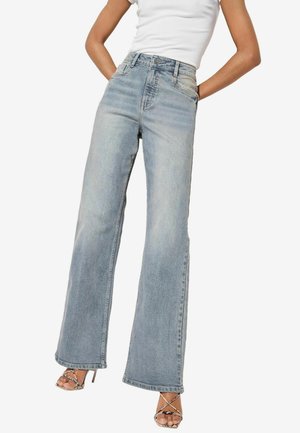 Jeans denim lebar berwarna biru muda dengan pinggang tinggi, dilengkapi dengan saku depan, dan hem yang frayed. Dipadukan dengan sandal hak tinggi bertali.