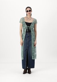 Dlouhý krajkový duster kabát v mentolově zelené barvě s krátkými rukávy, s předním zavazováním, vrstvený přes černý top a světle modrou deniminovou sukni.