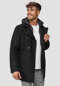 Svart pea coat med dobbeltradet knapper, notched krage og grå hette. Bært over en hvit skjorte, med lommer og teksturert fôr.