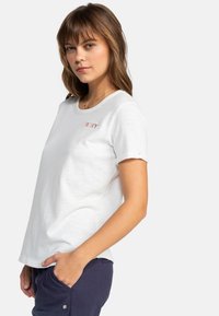 Camiseta blanca de manga corta con cuello redondo y "ROXY" bordado en rojo en el pecho. Tela suave y ligera con un ajuste relajado.