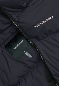 Giubbotto puffer blu scuro con una texture liscia. Presenta una chiusura zip frontale e il logo PeakPerformance visibile sul petto e sull'etichetta interna.