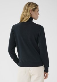 Black turtleneck sweater in a soft knit material with long sleeves and fitted design. Ribbed trim at collar and hem, worn with light-colored pants.