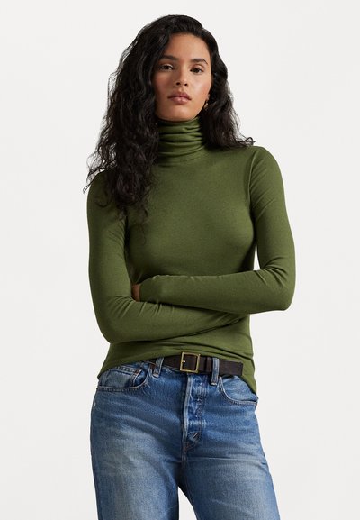 Vihreä ribatusta kankaasta tehty turtleneck-neule, slim fit -mallia, pitkät hihat. Yhdistetty sinisiin farkkuihin ja mustaan vyöhön, jossa on neliönmuotoinen solki.