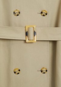 Tissu beige avec une ceinture assortie comportant une boucle rectangulaire en écaille de tortue et quatre boutons ronds en écaille de tortue disposés par paires.