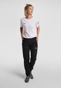Vit t-shirt med rund halsringning och svart logotyp, kombinerad med svarta joggers med elastisk midja som har en liten logotyp och sidofickor.