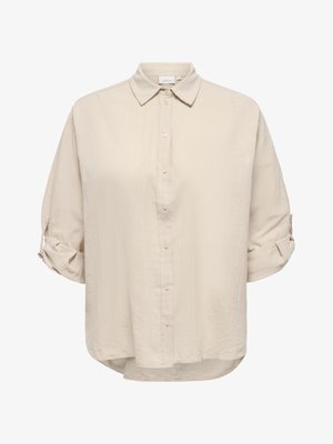 Beige nappipaita, jossa käännetyt hihat ja klassinen kaulus, teksturoitu kangas ja kevyesti kaartuva helma.