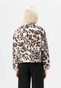 Chaqueta acolchada en crema con manchas abstractas marrones, con mangas de gran tamaño, un corte cropped y un acabado texturizado.