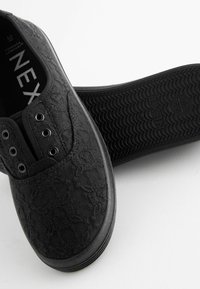 Schwarze, gemusterte Slipper aus strukturiertem Stoff mit fünf Ösen und einer strukturierten Gummisohle, innen mit dem Label "NEXT".