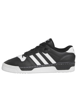 Sneakers Adidas basse noir et blanc avec trois bandes blanches, lacets noirs et semelle blanche épaisse sur un fond uni.