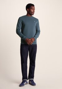 Teal sweatshirt with a crew neckline and ribbed cuffs, paired with dark jeans and blue sneakers with white stripes. No patterns or accents.