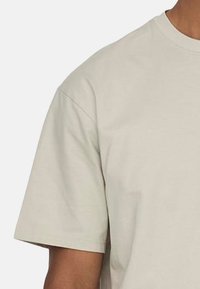 Helles beige T-Shirt mit kurzen Ärmeln aus Baumwolle. Hat einen Rundhalsauschnitt und eine lässige Passform. Der Stoff wirkt weich und glatt in der Textur.