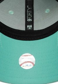 Mintgrüner Baseballcap-Innenraum mit einem schwarzen Band, das über einem glatten Untergrund mit einem weißen Aufkleber und rotem gesticktem Design verfügt.