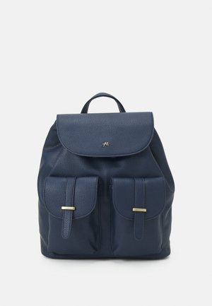 Marineblauwe leren rugzak met bovenklep, twee voorzakken met riemsluitingen, en een klein goudkleurig logo op de klep.
