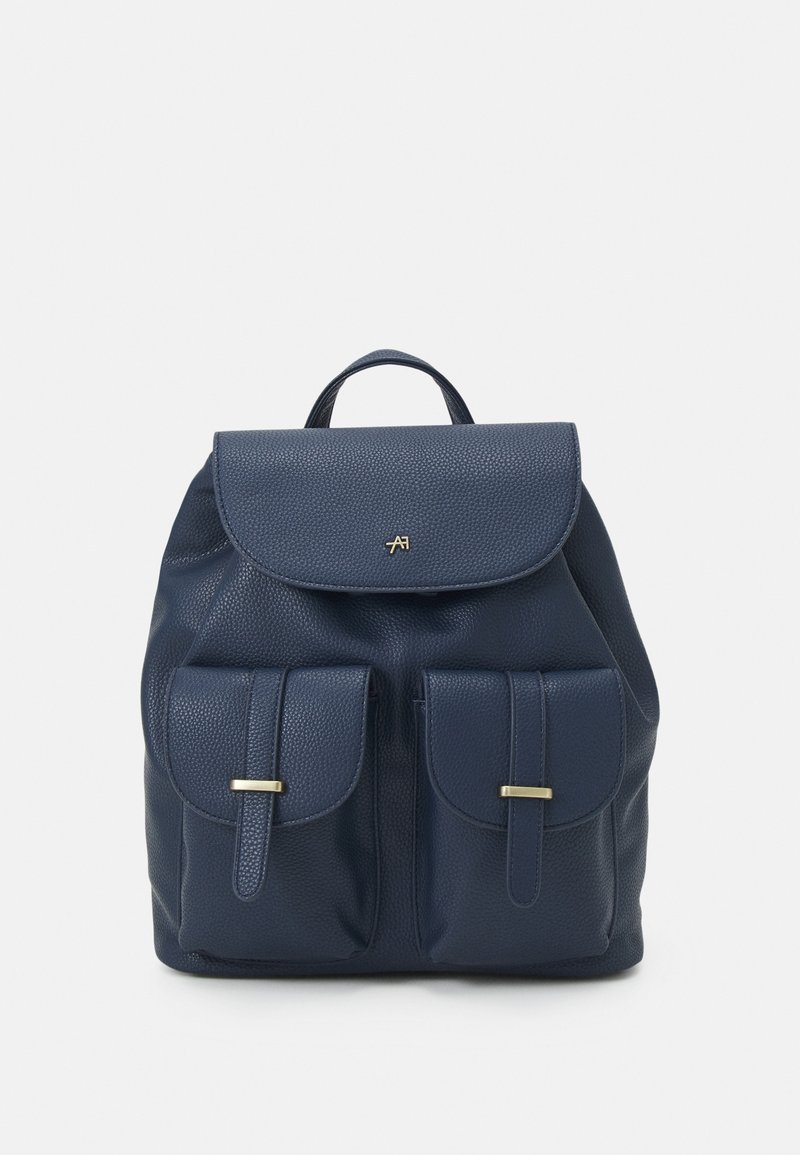 Sac à dos en cuir bleu marine avec rabat supérieur, deux poches avant avec fermetures par brides, et un petit logo doré sur le rabat.
