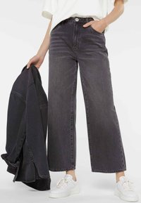 Wide-leg, dark grey jeans made of denim with a high waist, front pockets, and a button closure; paired with a matching jacket and white sneakers.