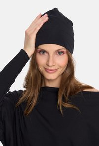 Czarna dzianinowa czapka z czubkiem, dopasowany fason i gładka faktura, noszona z luźnym czarnym topem. Charakteryzuje się swobodnym krojem i długimi rękawami.