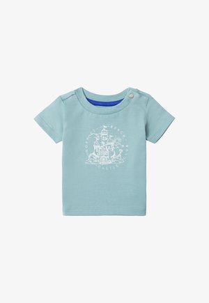 T-shirt en coton bleu clair avec un graphique de château blanc et le texte "Beach Club". Il a des manches courtes et une fermeture à bouton pression sur l'épaule.