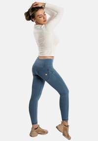 Leggings en denim bleu avec une taille haute, présentant un design traditionnel à 5 poches et un subtil logo doré sur la poche arrière.