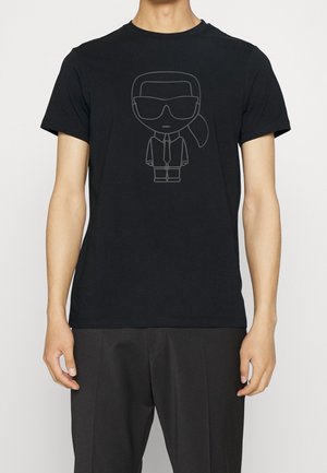 Musta puuvillainen t-paita, jossa on grafiikka hahmosta aurinkolaseissa, puvussa ja solmiossa. Päällä on sileä pinta ja rento istuvuus.