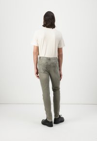 Jeans gri deschis cu o croială slim, asociate cu un tricou crem, prezentate din spate. Caracteristici: patru buzunare și un material texturat.