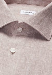 Col de chemise en lin beige clair avec boutons blancs et une étiquette de marque "seidensticker" visible à l'intérieur du col.