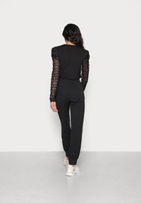 Czarny kombinezon z długimi koronkowymi rękawami i dopasowaną sylwetką. Posiada elastyczne mankiety, pasek w talii i zwężane nogawki. Noszony z białymi trampkami.