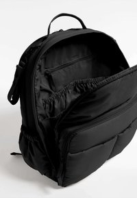 Crna ruksak s više pregrada, mekane teksture, s jastučićima i unutarnjim džepom s patentnim zatvaračem. Elastične džepove za organizaciju.