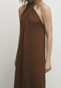 Robe marron à col licou en tissu doux, présentant un design drapé avec un col torsadé et des épaules dénudées, créant une silhouette décontractée.