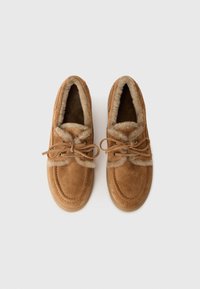 Een paar bruine suède moccasin slippers met een voering van bont en veters, vanuit bovenaf getoond op een witte achtergrond.