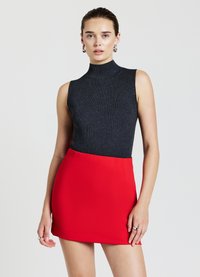 Top smanicato nero a coste con collo alto, abbinato a una minigonna rossa aderente, caratterizzata da una texture liscia e linee pulite.