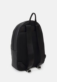 Black backpack features a smooth leather base with a textured mesh back panel and padded shoulder straps. Silver hardware accents.