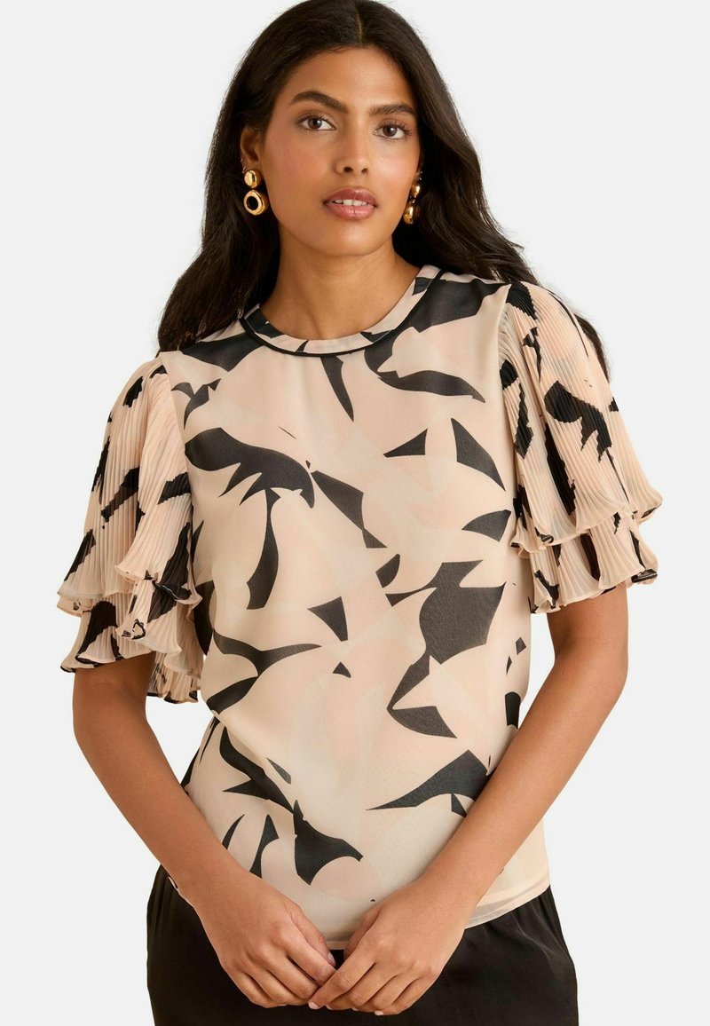 Kerge bluus, millel on beež põhivärv ja abstraktsed mustad mustrid. Puffvarrukad on volditud detailideks, et lisada tekstuuri.