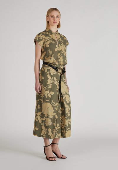 Robe florale verte à manches courtes, avec un col boutonné et une ceinture noire. Présente des motifs floraux jaunes, un design longueur cheville et des sandales plates.