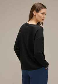 Felpa nera con vestibilità ampia, scollatura rotonda e maniche lunghe. Dettagli del logo evidenti sul retro vicino al collo. Texture liscia.