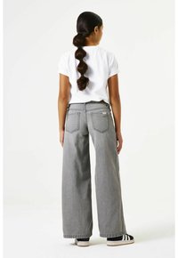 Grijze wijduitlopende jeans met een hoge taille, voorzien van achterzakken en een subtiel stiksel detail. Gecombineerd met een simpel wit T-shirt.