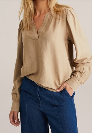 Beige blouse met lange mouwen, een V-hals en licht opgepofte schouders, gecombineerd met donkeblauwe denim broek met een losse pasvorm en zakken.