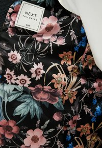 Czarna tkanina w kwiatowy wzór z różowymi, fioletowymi i niebieskimi kwiatami, z przymocowaną metką z napisem "NEXT TAILORING, 40R."