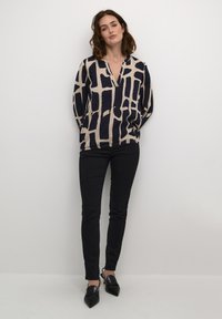 Losse, lange mouwen blouse in crème met donker marineblauwe geometrische patronen, gecombineerd met zwarte skinny jeans en zwarte schoenen met puntige neuzen.