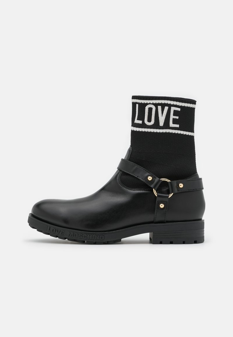 Bottine noire avec une partie inférieure en caoutchouc et un dessus en tissu semblable à un chausson. Comprend une bande "LOVE", des accents en métal doré et une semelle épaisse.