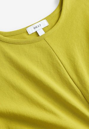Rövid ujjú, élénk lime zöld pamut felső, kerek nyakkivágással és finom varrással az elején. A "NEXT" márkajelzés látható.
