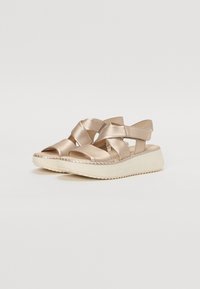 Sandali wedge metallici dorati con cinghie incrociate, suola imbottita e suola esterna in gomma testurizzata. Presentano una vestibilità ampia e un design elegante.