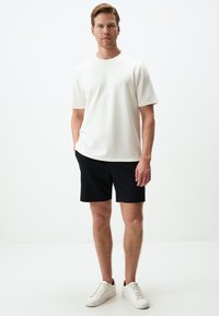 T-shirt blanche à manches courtes, shorts noirs et baskets blanches. Le t-shirt a un col rond, tandis que les shorts ont un design simple et ajusté.