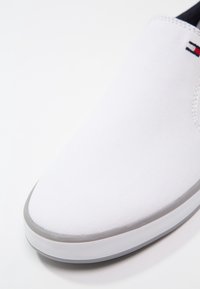 Scarpa slip-on bianca in tela con tomaia testurizzata, suola grigia in gomma e discreto dettaglio del logo sul lato.