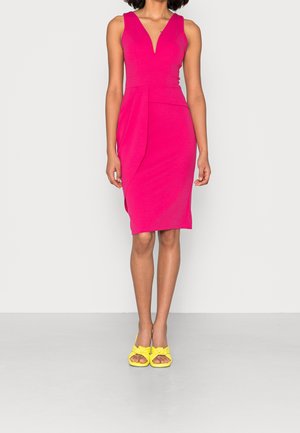 Mouwloze fuchsia jurk tot op de knie met V-hals en zijdetail met plooien, gecombineerd met gele open schoenen met strik.