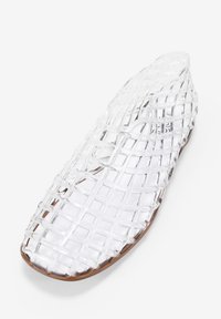 Zapato de plástico transparente tipo slip-on con un diseño trenzado, puntera redonda y suela de color marrón claro. La parte superior es completamente transparente.