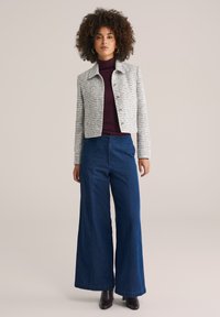 Grau karierte Jacke mit Kragen und vorderer Knopfleiste, kombiniert mit hoch taillierten, weiten blauen Jeanshosen und schwarzen Stiefeletten.