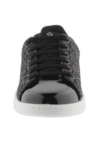 Schwarzer Sneaker mit strukturiertem Obermaterial, Schnürverschluss und glänzenden Lacklederakzenten. Weiße Gummisohle mit strukturiertem Muster.