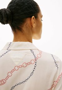 Hvid skjorte med et kædemønster i marineblå og røde nuancer, med en klassisk krave og et V-formet detalje på ryggen. Glat stoffel.