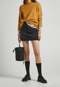 Pull en tricot orange, jupe en denim noir, chaussettes noires montant aux genoux et mocassins en cuir verni noir. Comprend un sac seau noir avec un détail matelassé.