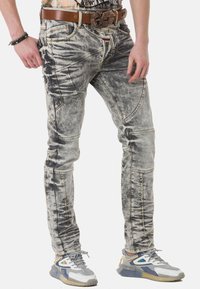Verwaschene graue Jeans aus Denim im tapered Fit, mit einzigartigen Stichmustern, seitlichen Taschen und einem braunen Leder Gürtel mit einer Schnalle.